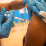 Person administering injection wearing blue gloves